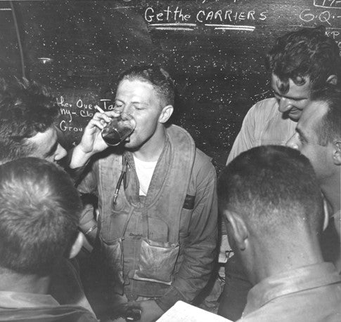 Lieutenant Ronald P. Rip Gift relaxes with other pilots in a ready room on board USS Monterey (CVL-26), after landing on her at night following strikes on the Japanese fleet, 20 June 1944. Note admonition on chalkboard in the background.
